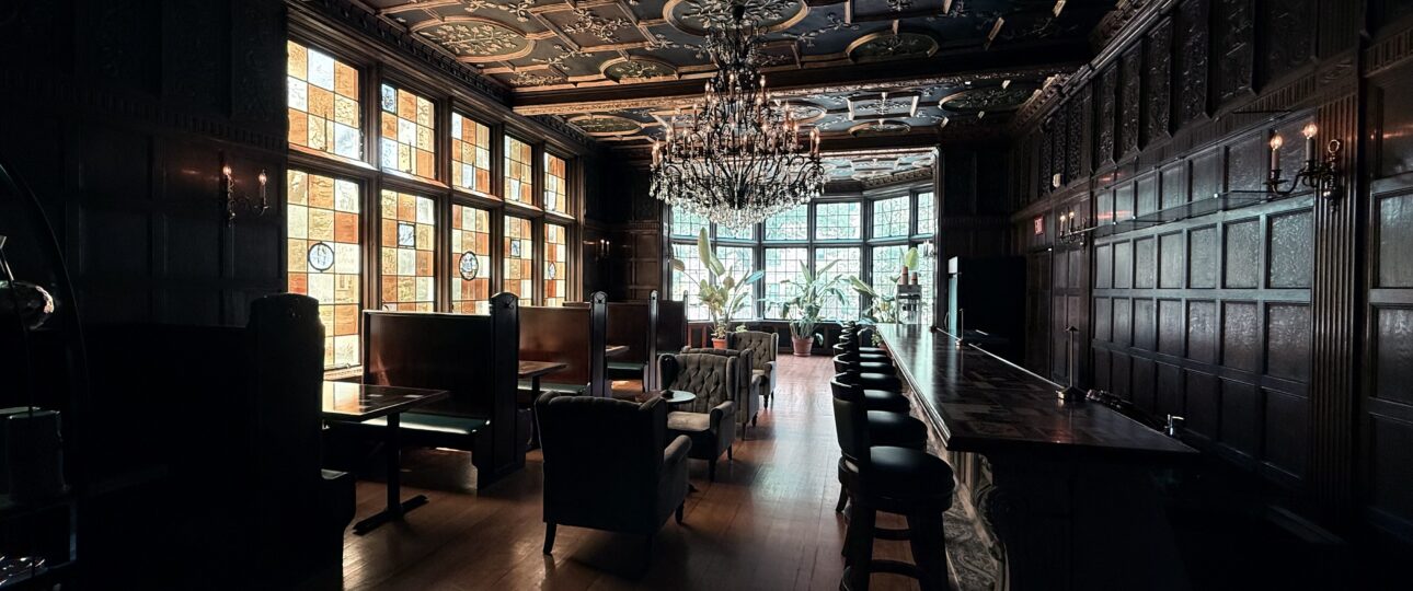 The dimly lit speakeasy-style bar room at the Pillsbury Club in Minneapolis, with carved oak paneling, stained glass windows and a chandelier.