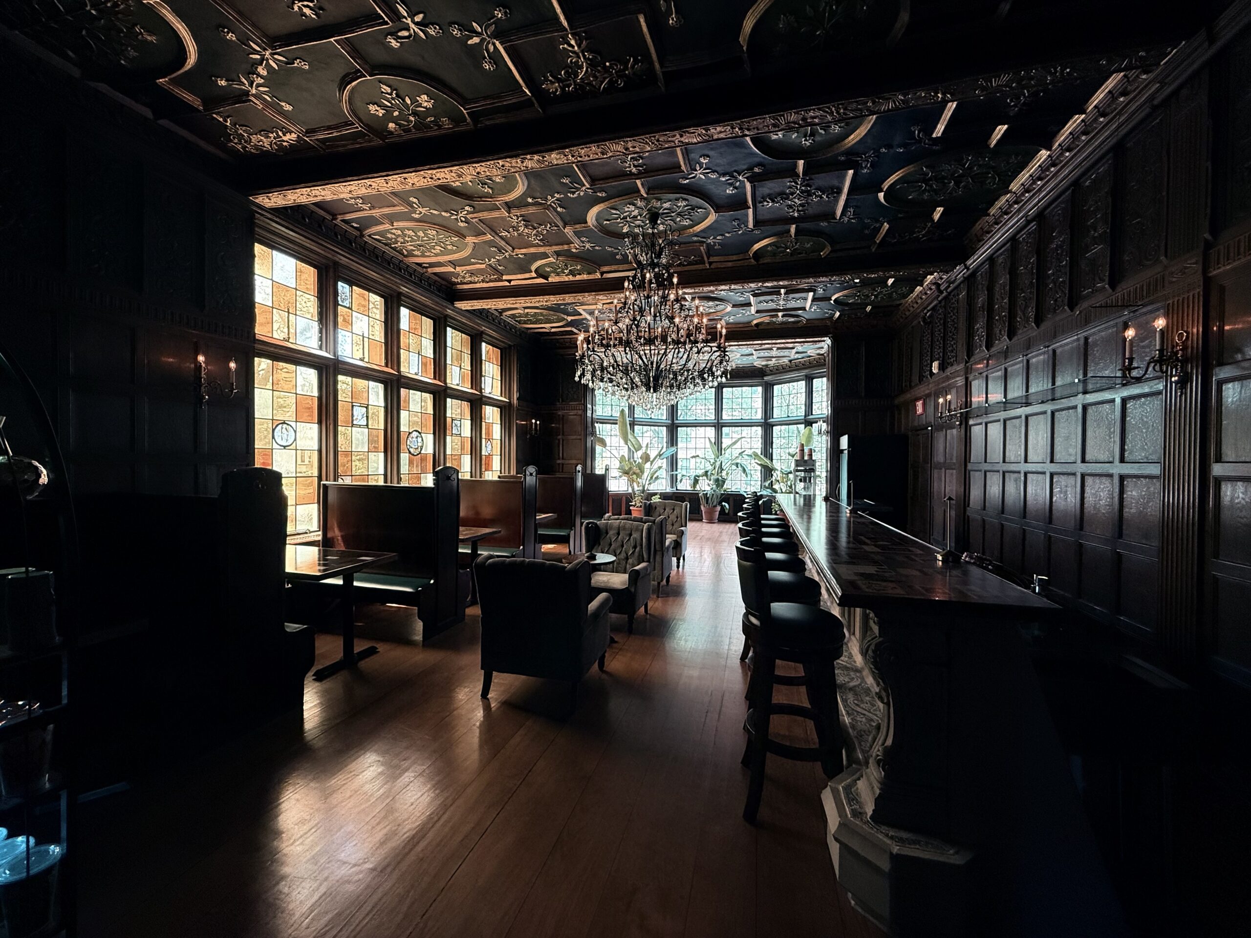The dimly lit speakeasy-style bar room at the Pillsbury Club in Minneapolis, with carved oak paneling, stained glass and a chandelier overhead.