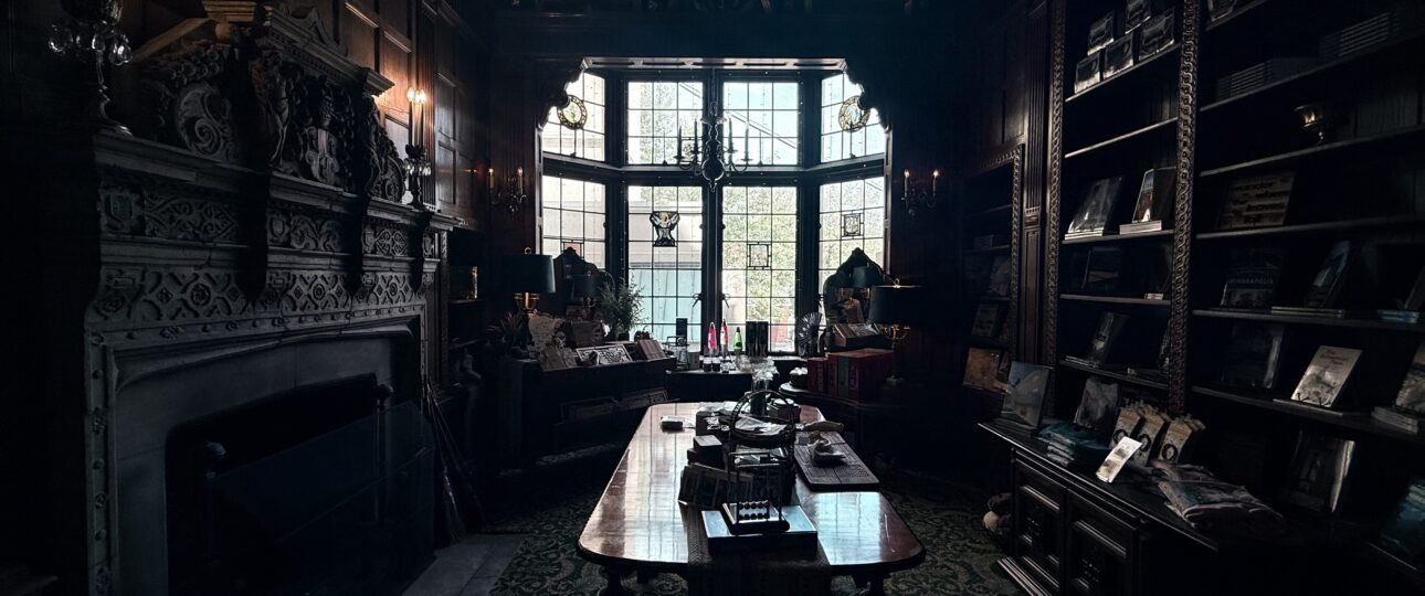 A dark oak-panelled club room inside the Pillsbury Mansion, with a carved stone chimneypiece and a long table set beneath leaded windows.