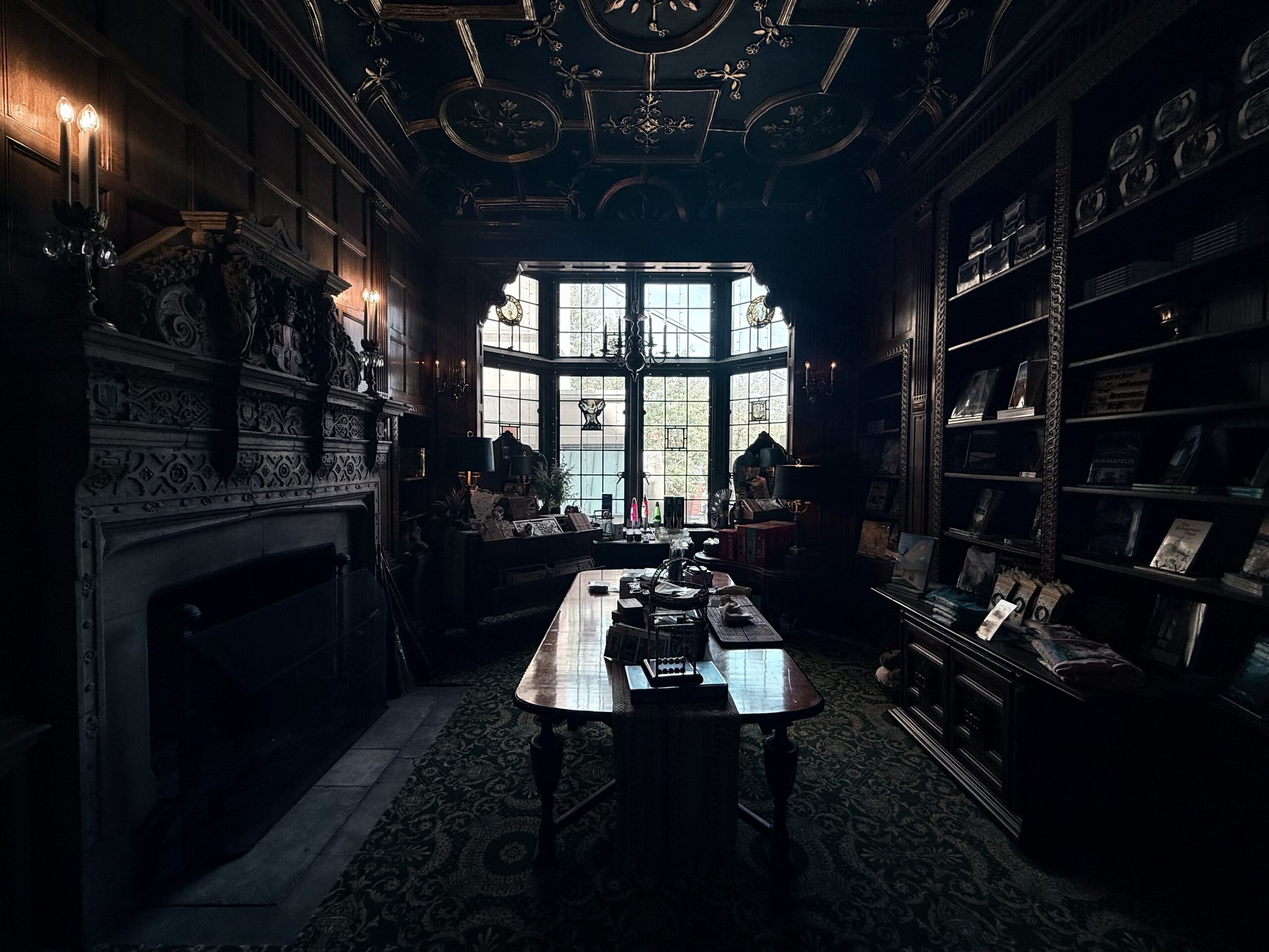 A dark oak-panelled club room inside the Pillsbury Mansion, with a carved stone chimneypiece and a long table set beneath leaded windows.