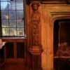 The carved stone chimneypiece in the library of the Pillsbury Mansion, flanked by carved oak figures and lit by leaded glass, bearing the Tallow Chandlers guild arms granted in 1456.