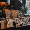 A display table in the Pillsbury Club Market in Minneapolis holding laser-cut wooden Minnesota keepsakes, kraft paper gift bags and a carved wooden box beside a leaded window