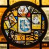 A leaded stained glass roundel in a Pillsbury Mansion window: a heraldic shield, a crowned lion, a helmeted figure, a bearded man in a ruff and the date 1636.