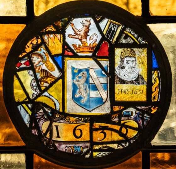 A leaded stained glass roundel in a Pillsbury Mansion window: a heraldic shield, a crowned lion, a helmeted figure, a bearded man in a ruff and the date 1636.